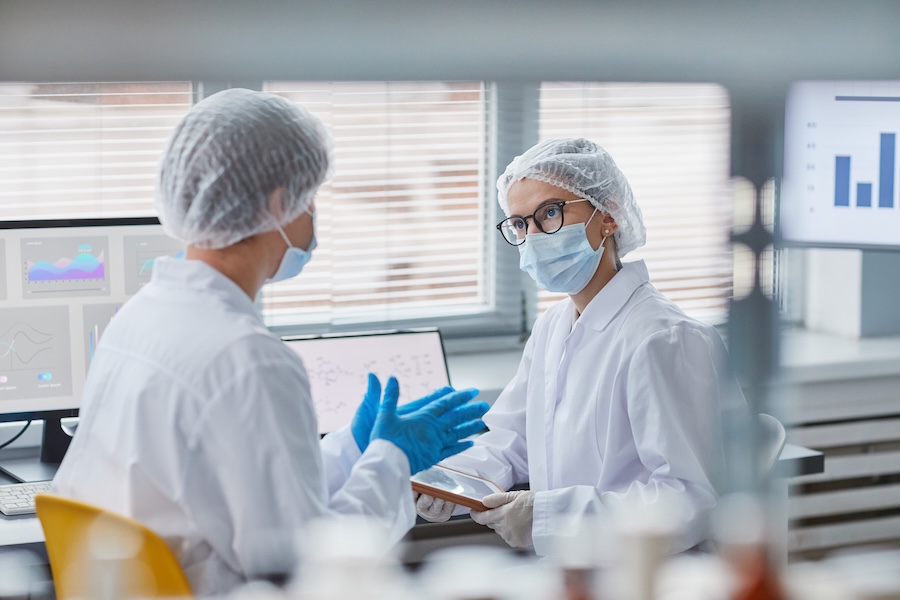 Two scientists in protective workwear talking to each other during their work in the laboratory